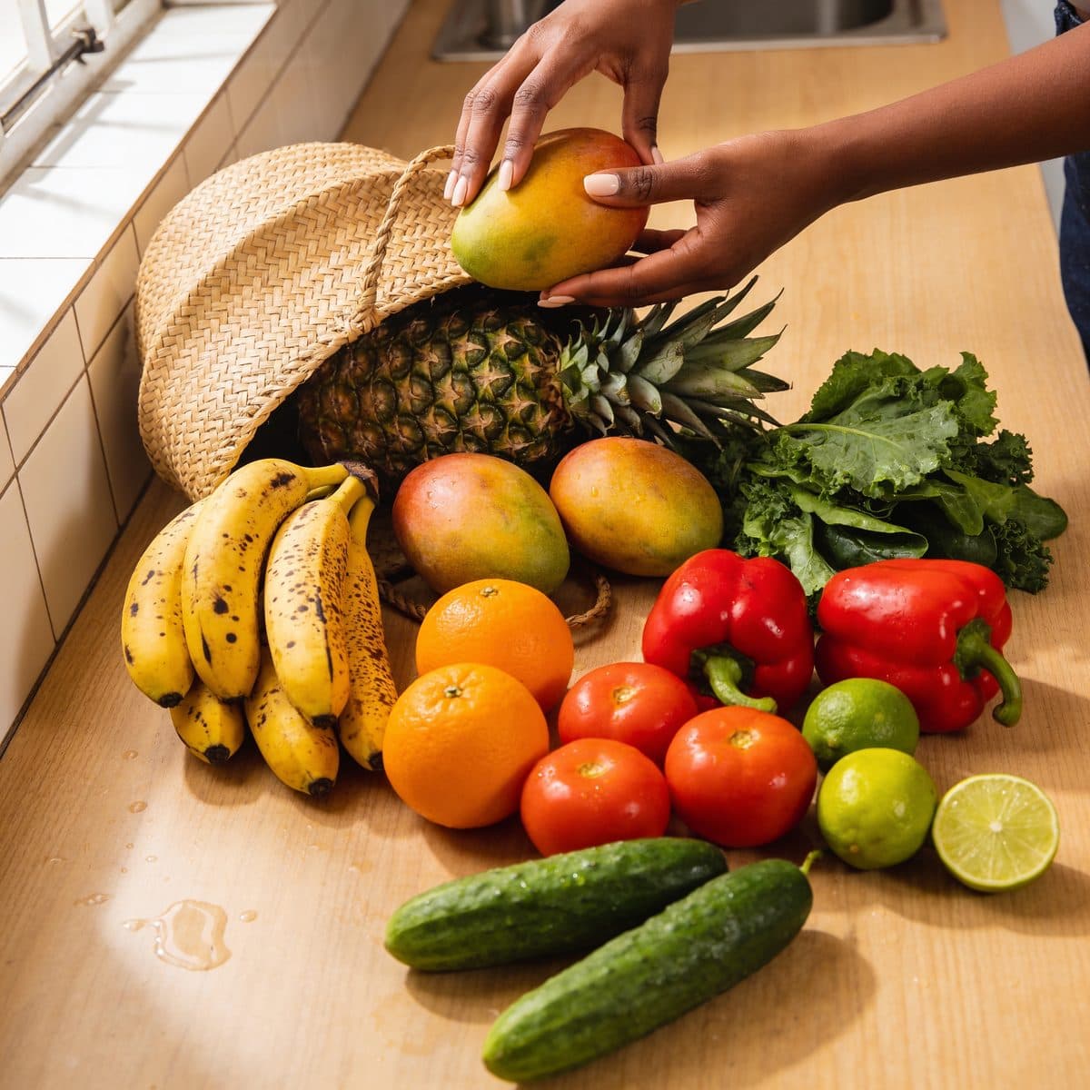 Pineapple, mangoes, plantain and greens being unpacked on a kitchen counter
