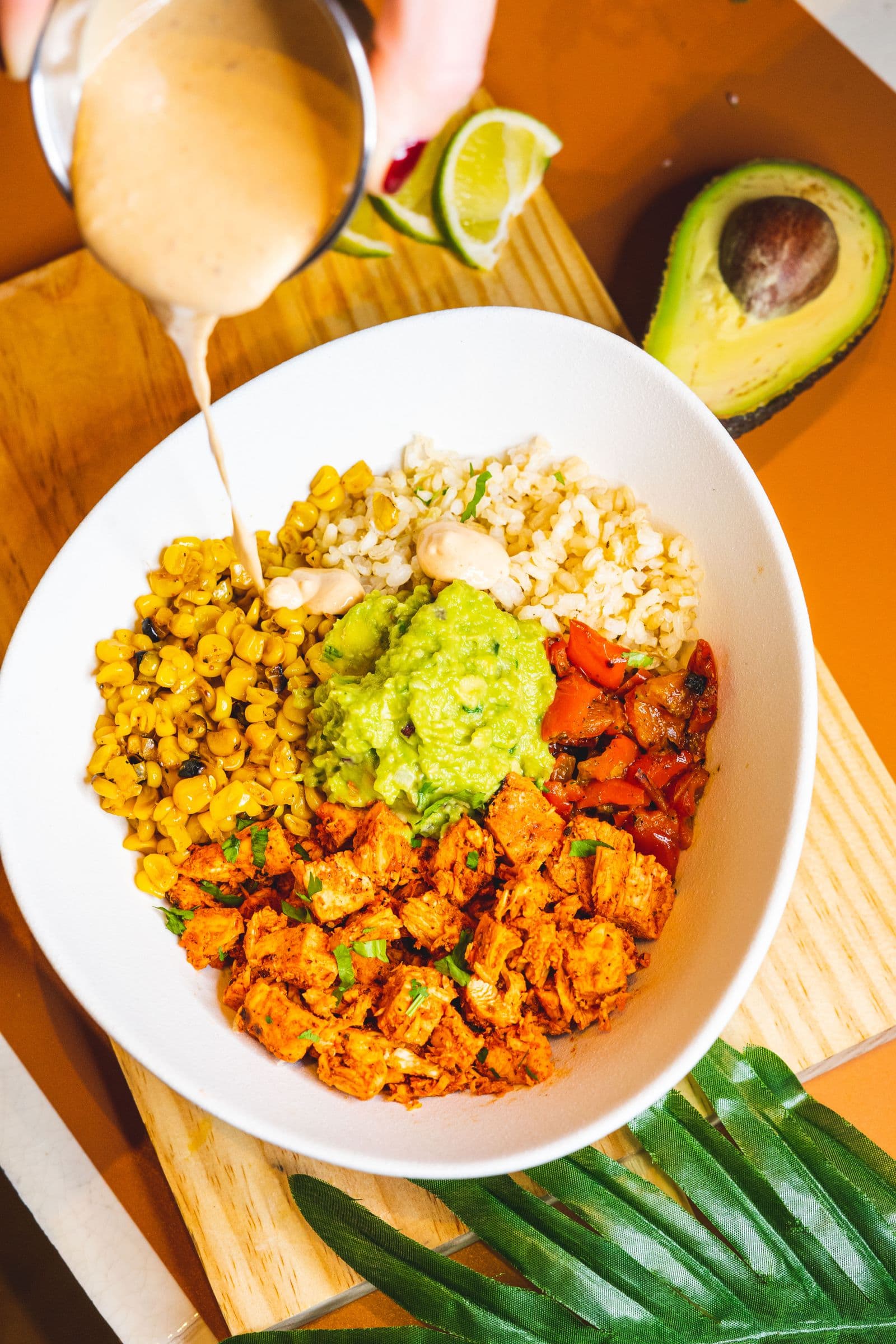 A burrito bowl with rice, guacamole, roasted vegetables and corn